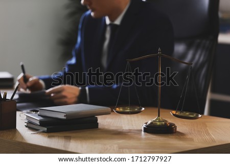Male lawyer working at table in office, focus on scales of justice