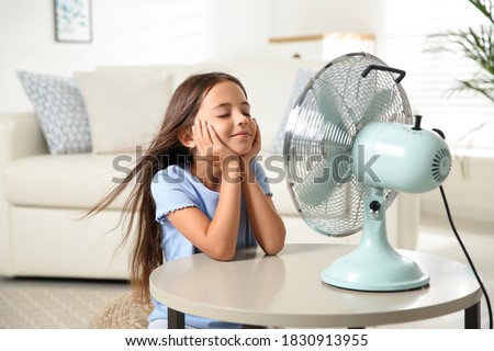 Little girl enjoying air flow from fan at home. Summer heat