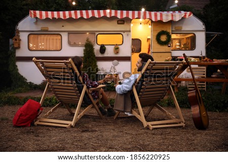 Young couple toasting with bottles of beer near trailer. Camping season