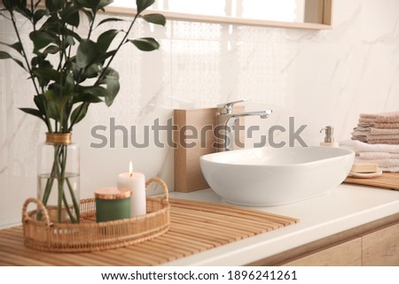 Vase with beautiful branches, candles and fresh towels near vessel sink in bathroom. Interior design