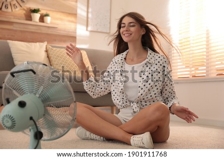 Woman enjoying air flow from fan on floor in living room. Summer heat
