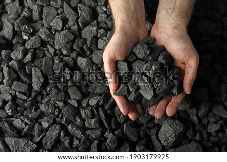 Man holding coal in hands over pile, top view. Space for text