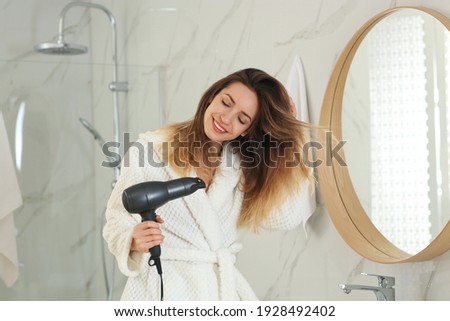 Beautiful young woman using hair dryer near mirror at home