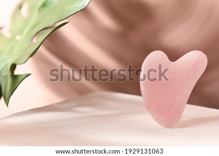 Rose quartz gua sha tool and tropical leaf on table, space for text Foto stock © 