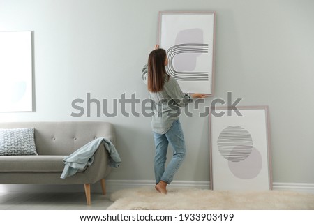 Woman hanging picture on wall in room. Interior design Stockfoto © 