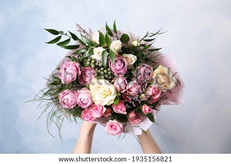 Woman with bouquet of beautiful roses on light blue background, closeup