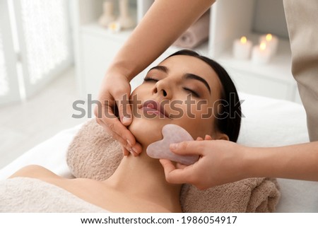 Young woman receiving facial massage with gua sha tool in beauty salon Foto stock © 