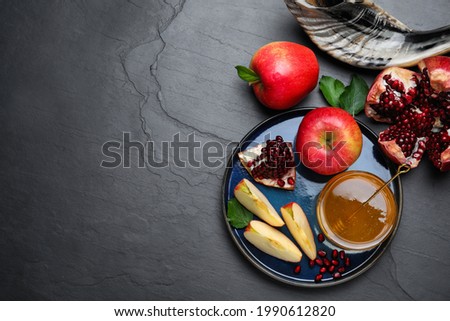 Honey, pomegranate, apples and shofar on black table, flat lay with space for text. Rosh Hashana holiday