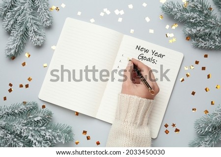 Woman writing in notebook at light grey table with Christmas decor, top view. New Year aims Foto d'archivio © 