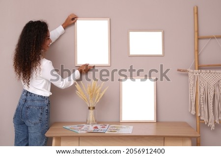 African American woman hanging empty frame on pale rose wall over table in room. Mockup for design Foto stock © 