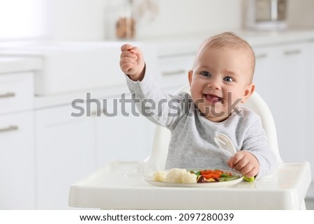 Similar – Image, Stock Photo Baby seated in high chair reaching for spoon; dramatic natural lighting and messy tray table