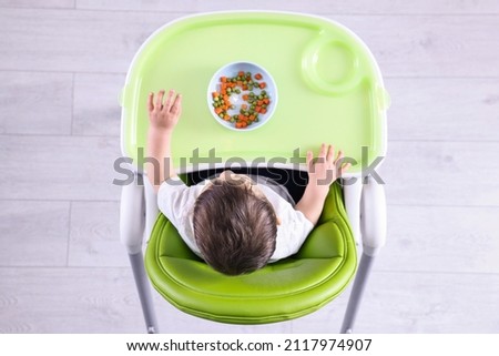 Similar – Image, Stock Photo Baby seated in high chair reaching for spoon; dramatic natural lighting and messy tray table