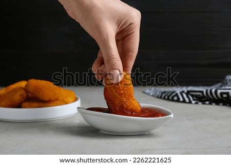 Woman dipping delicious chicken nugget into ketchup at light grey table, closeup Foto stock © 