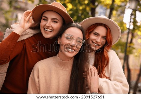 Foto Bild Lächelnde Freundinnen mit Hüten unterhalten sich auf einem Holzzaun am Strand sitzend