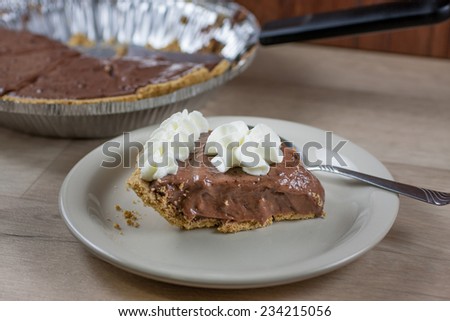 Chocolate cream pie on a white plate with the rmaining pie in the background.