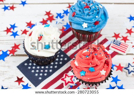 Chocolate cupcakes decorated in red, white, and blue and surrounded by stars and flags in celebration of  Independence Day.