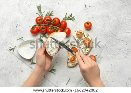 Woman making tasty sandwich with cream cheese on white background