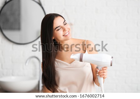 Beautiful young woman with hair dryer in bathroom