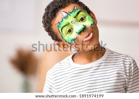 Funny African-American boy with face painting at home