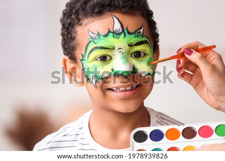 Woman painting face of African-American boy at home