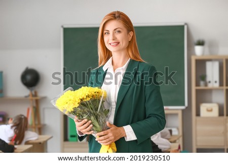 Beautiful teacher with bouquet of flowers in classroom