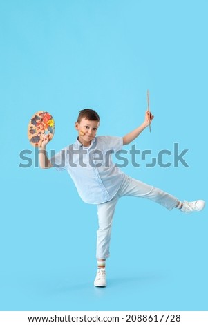 Cute little boy with paint palette and brush on color background