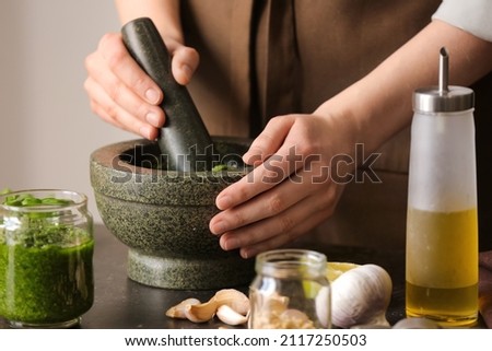 Woman making pesto sauce with mortar and pestle on table in kitchen Stockfoto © 