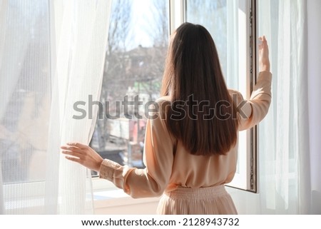 Pretty young woman opening window in room Imagine de stoc © 