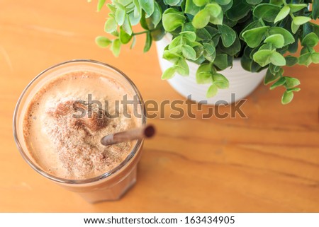 Cocoa milkshake on wood table with artificial plant (bird\'s eye view)