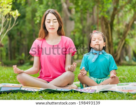 Mother and daughter doing yoga outdoors - mother teaching her daughter how to do exercises.