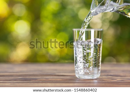 water from jug pouring into glass on wooden table outdoors Foto d'archivio © 