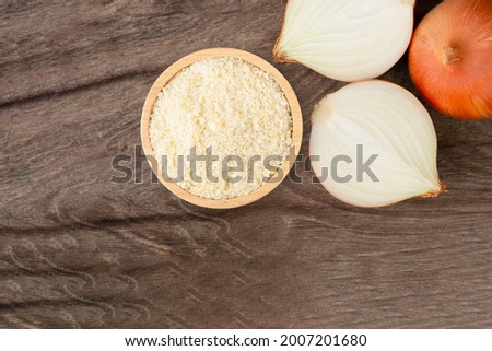 Ground onion or onion powder in wooden bowl and fresh onion with half sliced isolated on wooden table background. Top view. Flat lay.