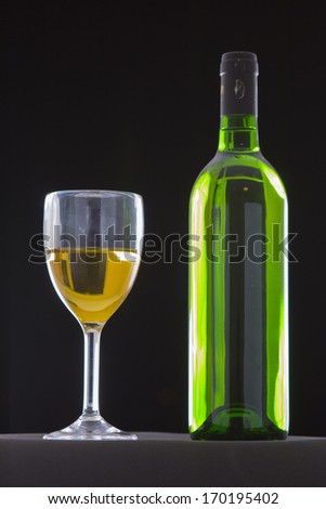 White wine bottle and glass on black grounds.