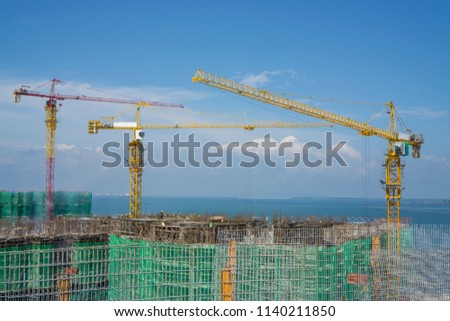 Tower crane on top of a large building in construction work, there're builder working on top floor, scaffolding on each story and cover by green net protection, sea on baclground under clear blue sky Stock foto © 