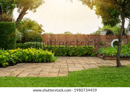 Back and front yard cottage garden, flowering plant and green grass lawn, brown pavement and orange brick wall, evergreen trees on background, in good care maintenance landscaping in park  Foto d'archivio © 