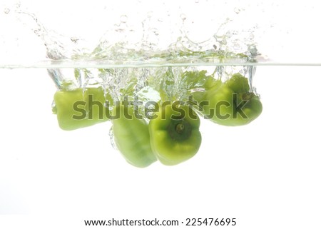 Close up green pepper fall into the water, white background.