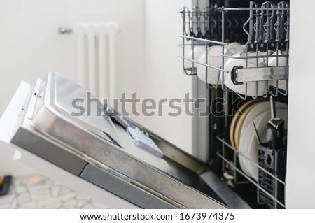 Open dishwasher with clean dishes in the white kitchen