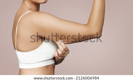 Close-up of a young tanned woman grabbing skin on her upper arm with excess fat isolated on a beige background. Pinching the loose and saggy muscles. Overweight concept Stockfoto © 