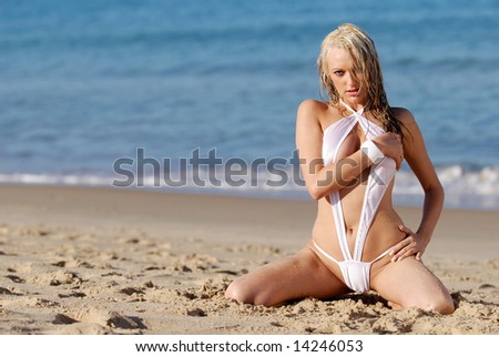 Sexy blonde woman in white bikini posing on beach.