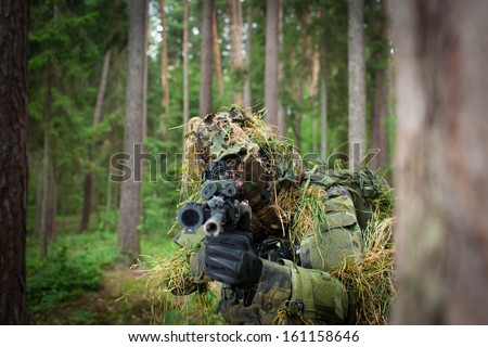 Masked soldier/sniper is aiming at the target during the mission (visible eye throught a telescope,color toned image)