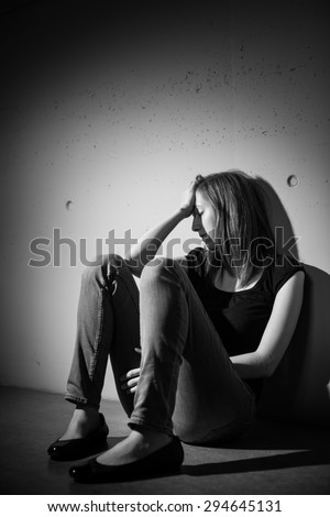 Young woman suffering from a severe depression, anxiety (very harsh lighting is used on this shot to underline the gloomy mood of the scene, black and white image)
