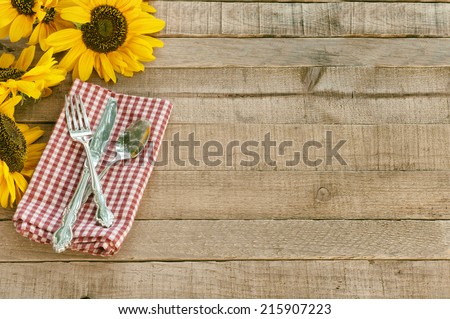 Picnic Table Setting with Pretty Cheerful Sunflowers, Silverware, red  white checked napkin, brown Rustic Wood Board Background, empty room or space for copy, text, your words.  Horizontal