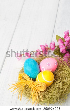 Pretty Easter Eggs in Nest with Pink Flowers in lower framework on Rustic White Wash Painted Board Background with empty, blank room or space for copy, text, your words.  Vertical above view