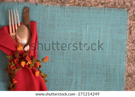 Fall or Summer Table Placesetting above view with Cloth Napkin, Fork, Knife, Spoon, Flower Ring on Cyan Burlap Mat on Stone Table with room or space for copy, text,  words.  Horizontal looking down
