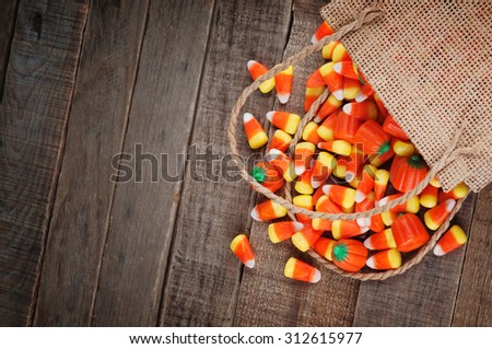Above view of Halloween candy corn spilling from a burlap bag on rustic wood board background with room or space for copy, text, your words.  Horizontal that works vertical with Moody, dark vignette
