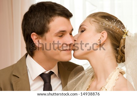 Wedding portrait of a newly-married couple. The bride kisses the groom