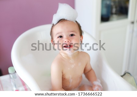 Top view of little cute baby take a bath and playing with foam bubbles with smiling face.mixed race Asian-German infant bathing in white bathtub laughing and fun. Happy child in bathroom. 商業照片 © 