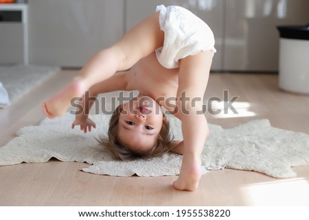 Cute and funny baby boy wearing diaper bending over doing yoga or playing hide and seek at home. Happy mixed race Asian-German child play and learn development.