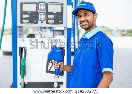 Happy petrol pump worker standing by holding fuel nozzle while looking camera at gas filling station - concept of happiness, job and petroleum service. Foto d'archivio © 