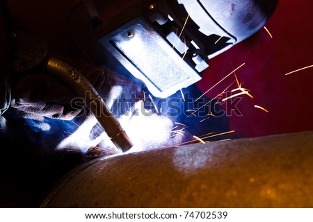 Welder with protective equipment weld metal pipes in factory